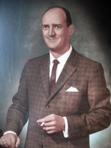 Color portrait of a man wearing a suit and tie, photographed against a studio backdrop