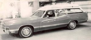Black-and-white photograph of a vintage Demers automobile ambulance parked outside a building