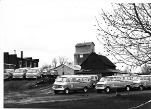 Black-and-white image of several Demers vintage ambulances parked outdoors near industrial buildings