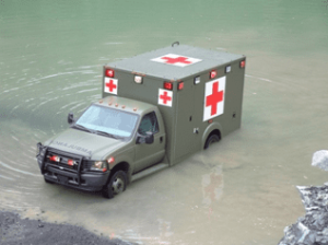 Demers ambulance driving through shallow floodwater with emergency markings visible