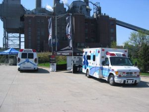 Two Demers ambulances parked outdoors in front of an industrial facility during an event