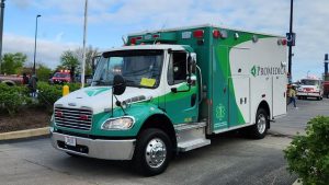 Green-and-white Demers ambulance on a roadway in an urban area