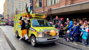 Demers ambulance driving through a city street during a parade with spectators along the sidewalk