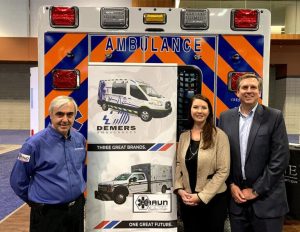 Three people standing in front of an ambulance-themed display with Demers and Braun branding