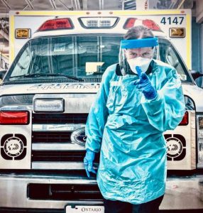 EMS responder wearing protective gear standing in front of a Demers ambulance