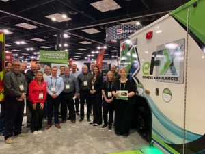Group of Demers team members standing beside an electric ambulance at a trade show